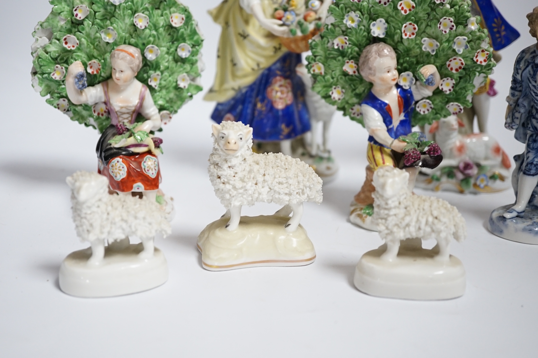 A pair of Derby style porcelain small bocage figures, a boy and girl seated with grape filled hats, height 14cm, three porcelain lambs and another figure